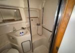 Compact beige bathroom with sink, mirror, toilet, and enclosed shower; bottles on the sink.