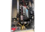 Marine boat engine inside the engine compartment, with red wiring, hoses, and a Mercury cover visible.