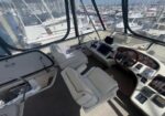 Luxurious yacht cockpit with beige captain's chair, helm station, and navigation screens inside a glass-enclosed bridge overlooking a marina.