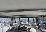 Front view from the helm of a motorboat, showing the steering wheel and navigation controls, looking out at a crowded marina with many moored boats.