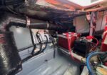 Cramped boat engine bay with a red marine battery, cables, and a black exhaust hose.