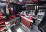 Boat engine room with red batteries in a tray, red cables, hoses, and electrical controls in a cramped space.
