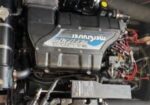Mercury MerCruiser marine engine with blue label, exposing hoses, wiring, and components in an engine bay.