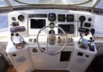 Boat helm with stainless steering wheel, multiple navigation screens, gauges, and radios.