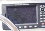Close-up of a Standard Horizon marine navigation display with a curved metal railing in the foreground.
