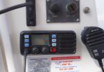 Maritime control panel with a small VHF radio and microphone, start/stop switch above, and navigation/switches on the left; the handheld mic rests to the right.