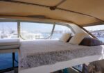 Luxurious yacht bedroom with a fluffy gray blanket, white pillows, and a view of the marina through large windows.
