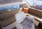 Sunlit boat cockpit with beige cushioned seating, an orange starfish-patterned pillow, and a white chair with a black-and-white spotted throw.