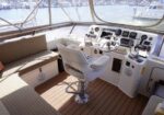 Captain's chair at a yacht's helm with gauges, steering wheel, and marina view through large windows