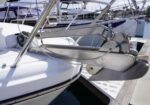 Close-up of a white sailboat at a dock, showing a stainless steel anchor mounted on the bow and boat hardware with other boats in the background.
