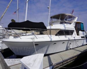 White motor yacht moored at a marina with a black cover over the forward deck and blue sky above.