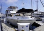 White motor yacht docked at a marina with a black cover over the bow; surrounding slips and a dock-side fuel pump nearby.