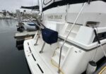 Rear of a white sailboat docked at a marina; mast and rigging visible, name on hull ends with '... BELLE', with a yellow cord and a fender on the stern.