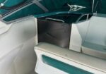 Interior of a small boat cockpit with white seats and teal accents, teal canvas canopy overhead, and a dark center console area behind the bench.