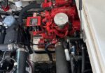 Red marine engine with hoses, clamps, and wiring in a compact boat engine bay (view from above). The red engine block is centered with a silver air-filter housing visible.
