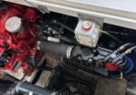 Engine bay showing a red engine block, white coolant reservoir, and a network of hoses and clamps from above (marine/industrial engine).