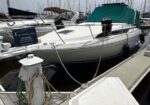 White motorboat docked at a marina with a green canopy, moored beside a white dock pedestal and coiled lines in the foreground.