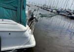 Rear view of a white sailboat with a green canvas cover docked at a marina, with other sailboats in the background.”] ,