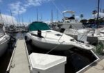 Marina with multiple white motor yachts docked along a wooden pier, mooring lines secure the boats under a blue sky with scattered clouds. One boat has a green cover on its cockpit.