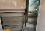 Cozy boat cabin with a beige seating area, wooden table edge, and carpeted stairs leading up to the deck.