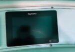 Raymarine marine display mounted on a boat console with a dark screen and a small control panel on the right.