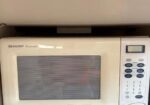 White Sharp Carousel microwave oven with a striped window and a right-side control keypad on a kitchen counter.