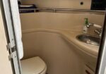 Compact bathroom with a toilet on the left and a curved sink on the right; beige walls, towel, and soap dispenser visible above the sink.