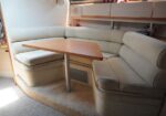 Cream-colored U-shaped seating area around a wooden rectangular table in a boat cabin, with storage cabinets above.