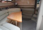 L-shaped cream sofa seating around a wooden boat table in a cabin, with stairs and compact storage nearby
