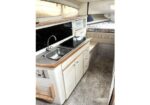 Compact camper kitchenette with sink, stove, microwave, and storage cabinets beside a bed area in an RV interior.