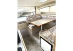 Compact boat cabin with a wooden dining table and U-shaped floral upholstered benches surrounding it