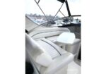 White leather boat cockpit seating with a small fold-out table, seen in a marina setting with windows and seating surrounding the area.