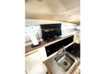 Compact boat galley with a flat-screen TV on the counter, a roll of paper towels, and a stainless steel sink with a small faucet.