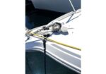 Close-up of the bow hardware on a white sailboat: winch, mooring lines, and a yellow line secured near the deck edge with water below.