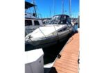 White motor yacht moored at a marina on a sunny day, tied to a wooden dock with sailboats in the background.