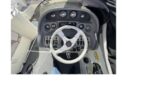 Top-down view of a boat helm: white steering wheel, analog gauges, switches, and throttle on the right.