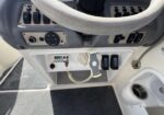 Boat helm area with steering wheel, control switches, and throttle levers on a console panel.