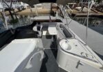 Deck of a white motorboat with seating and a small sink area, dock and marina visible in the background.