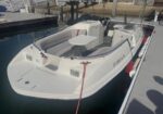 White motorboat docked at a marina with cushioned seating and a small folding table onboard.