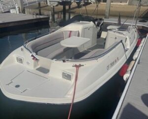 White motorboat docked at a marina with cushioned seating and a small folding table onboard.