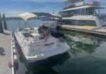 White motorboat moored to a wooden dock with a beige canopy, a small American flag, and a larger yacht in the background at the marina.
