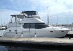 White motor yacht moored at a marina, featuring a covered upper deck and large windows on the hull.