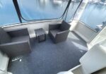 Wicker outdoor seating on a boat deck: two chairs and a small table, with a marina visible through glass walls.