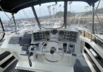 Boat cockpit with steering wheel and instrument gauges, marina visible through windshield.