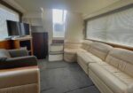 Cream leather sectional and armchairs in a boat lounge, with a TV on the left and steps to a door at the back.