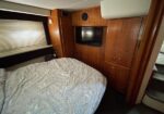 Wood-paneled bedroom in a boat/RV with a large bed, mounted TV, and tall storage cabinets on the wall.