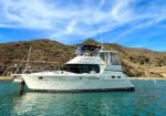 White motor yacht anchored in calm turquoise water with rocky hills in the background under a blue sky. (informative)