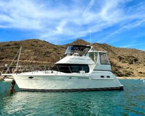 White motor yacht anchored in calm turquoise water with rocky hills in the background under a blue sky. (informative)