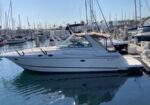 White motor yacht docked in a marina with sailboats in the background, calm water reflecting the hulls.