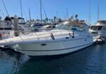 White motor yacht docked in a marina with other boats and masts in the background under a clear blue sky
